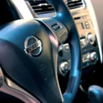 Kierownica Nissana z przyciskami i zegarami w tle, wnętrze auta Toyota w serwisie
